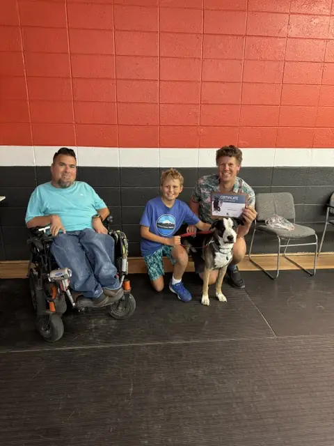 Jason Lake with a Basic Obedience graduate, a young family member, their black-and-white dog and graduation certificate at Prodogz in Medford, Oregon — photo 1
