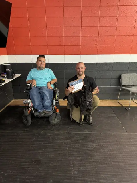 Jason Lake with a Basic Obedience graduate holding his certificate beside a dark-coated dog at Prodogz in Medford, Oregon — photo 5